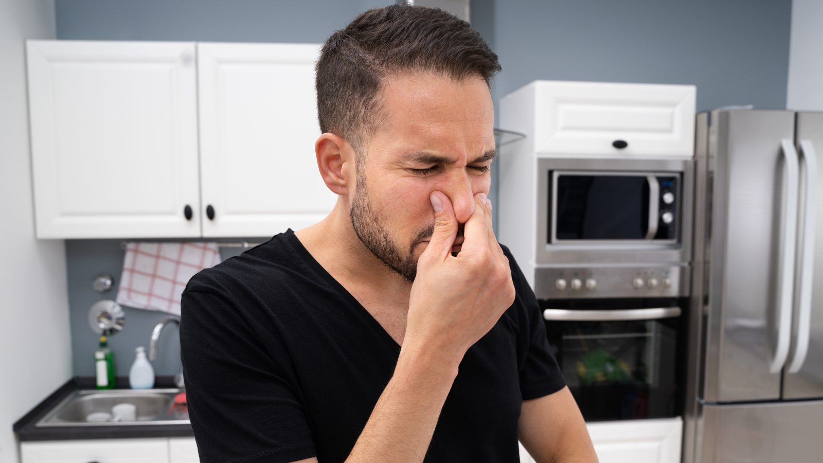 Man pinching his nose closed to keep out a bad smell in his kitchen.